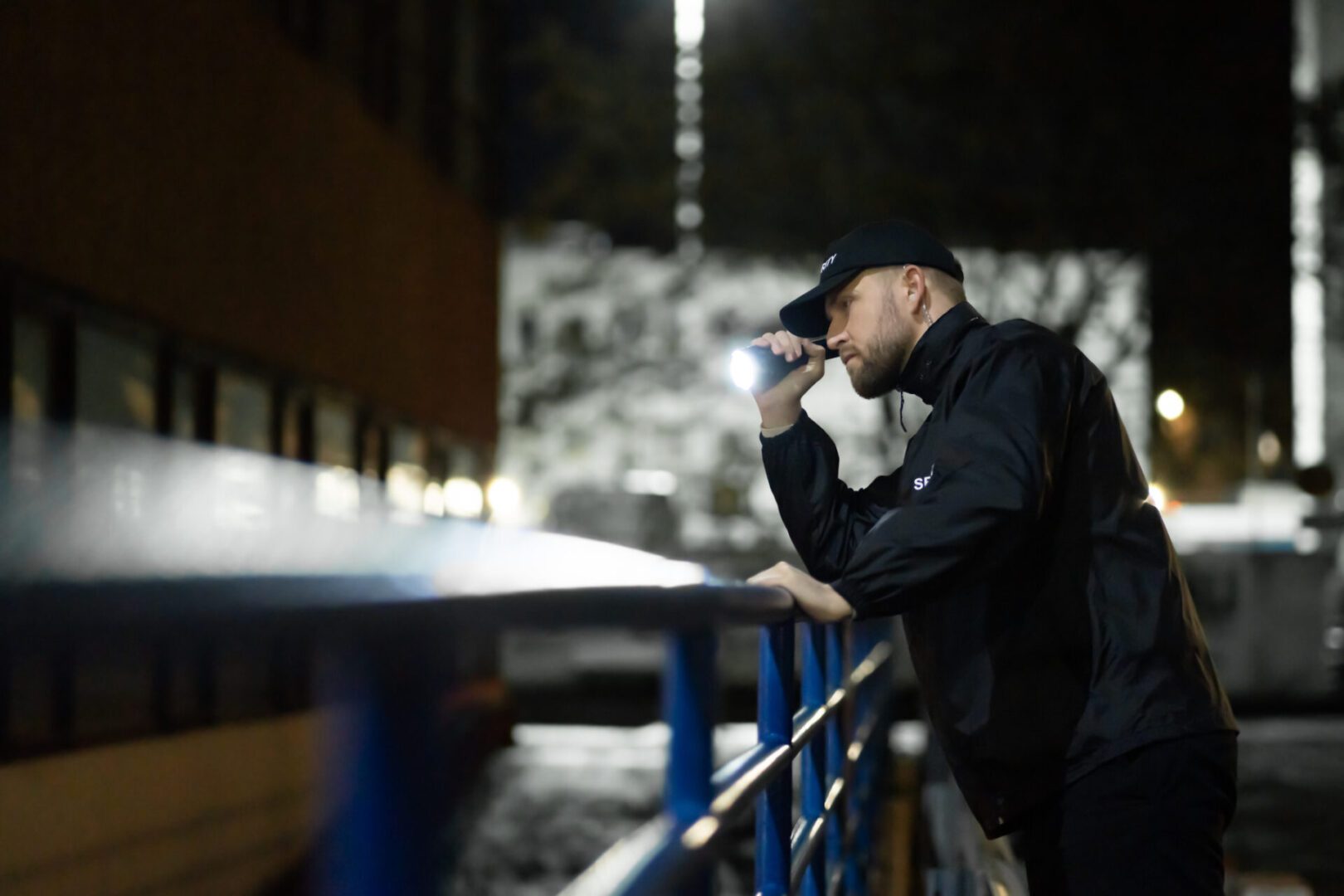 Security Guard Walking Building Perimeter With Flashlight At Night