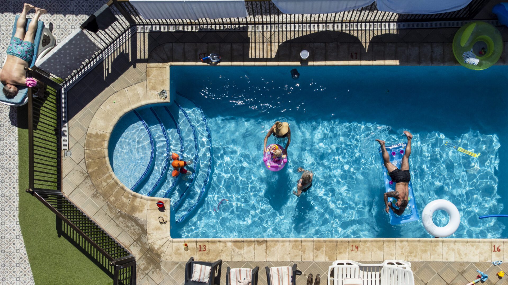 A directly above drone shot of a mixed age family in and around a swimming pool, they are having fun in the sun on vacation in Tenerife.