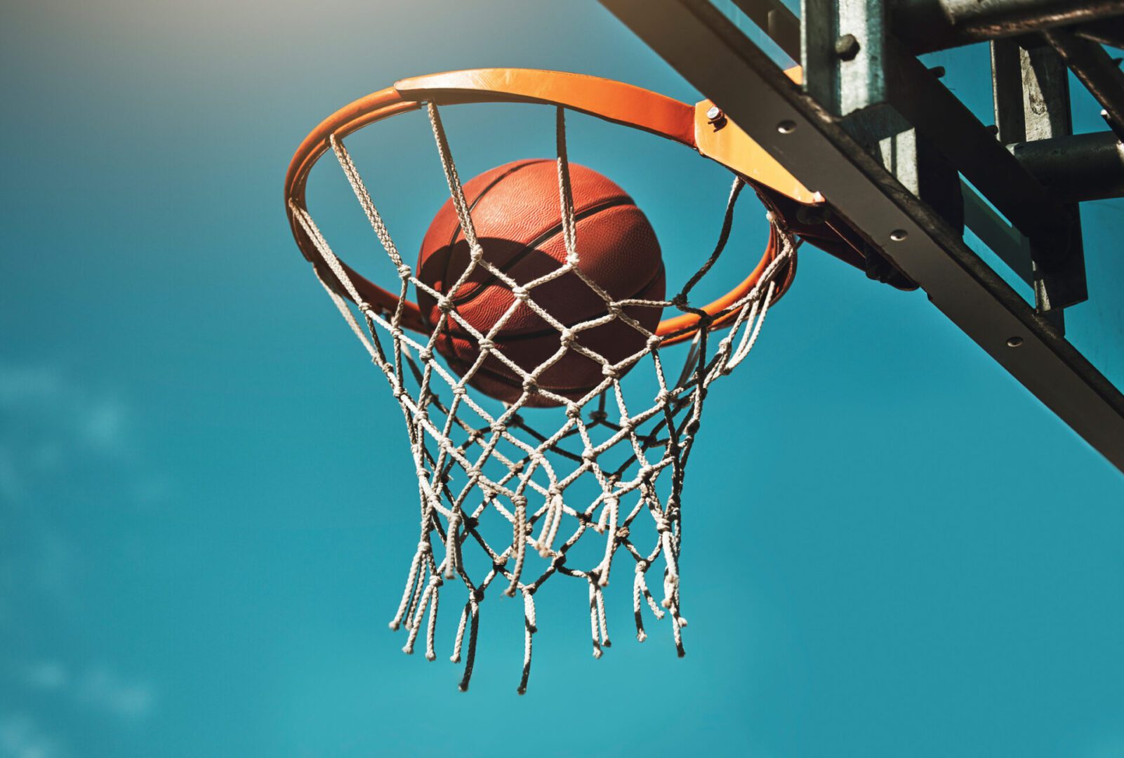 Basketball, goal and target in basket for sports match training on outdoor athletic court. Aim, score and winner with ball dunk in net at competition practice from low angle with blue sky.