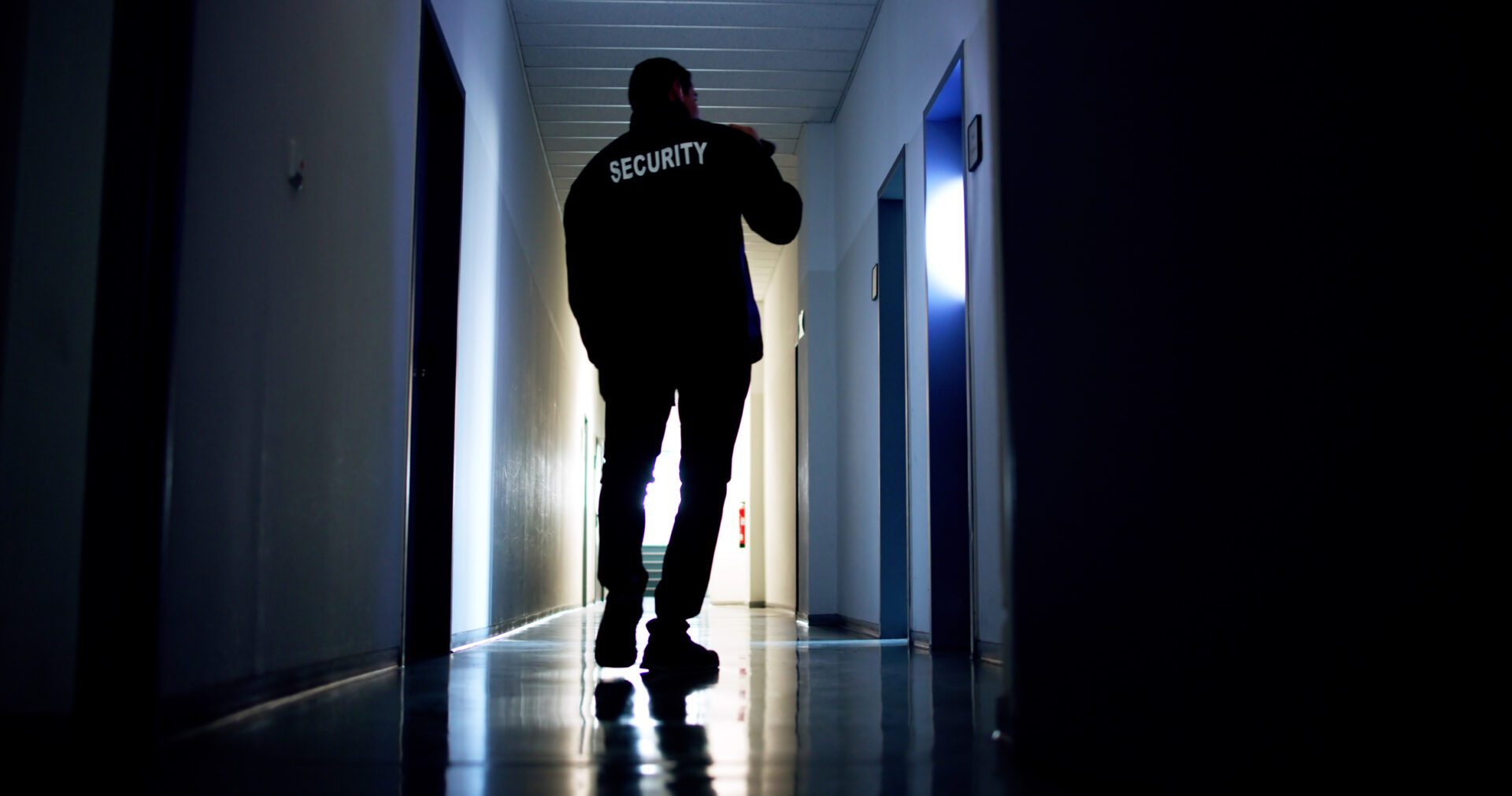 Security Guard Standing In Corridor Of The Building Using Flashlight