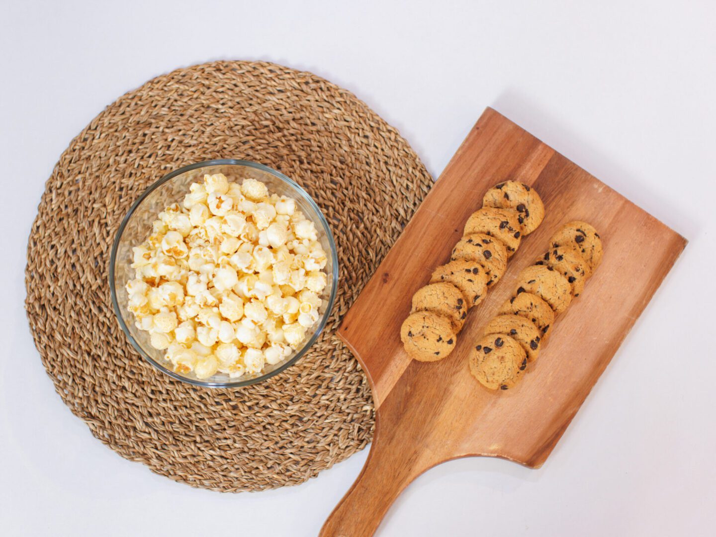 Top view chocolate chip cookies arranged on a wooden cutting board and popcorn in glass bowl snacks on white background, Party food concept.