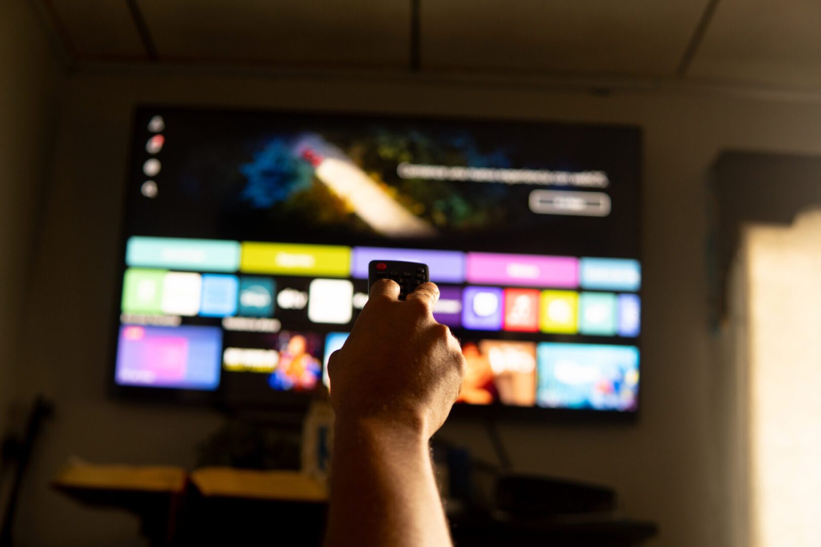 Hand holding remote control pointing at smart tv displaying streaming service menu in living room