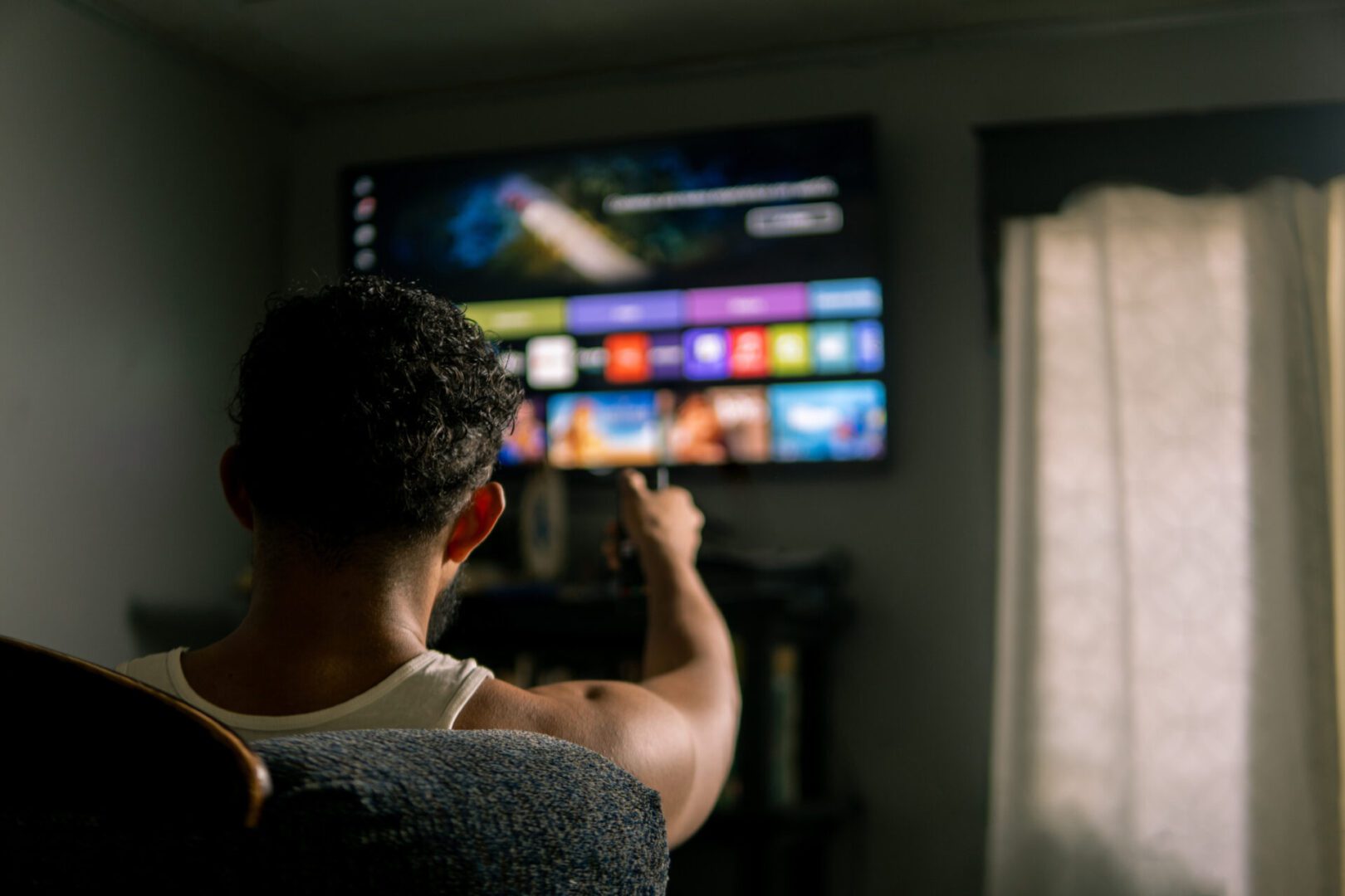 Young adult man using remote control, choosing streaming platform content on smart tv