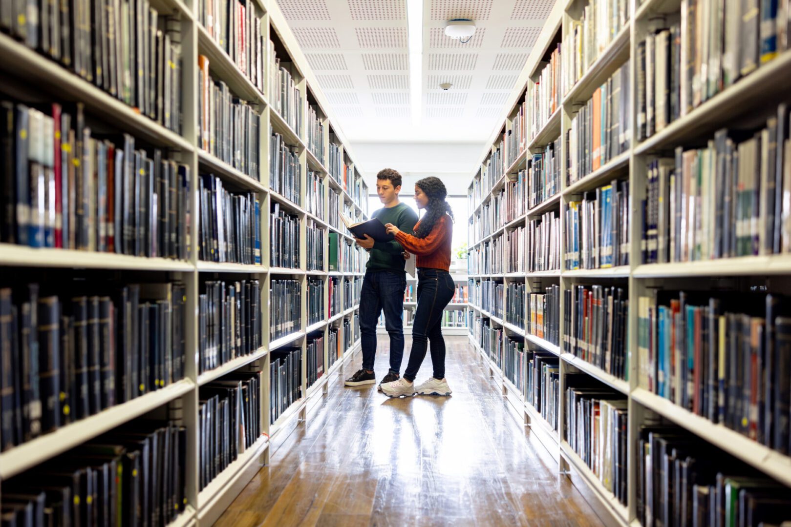 Two Latin American students searching for a book at the library - education concepts