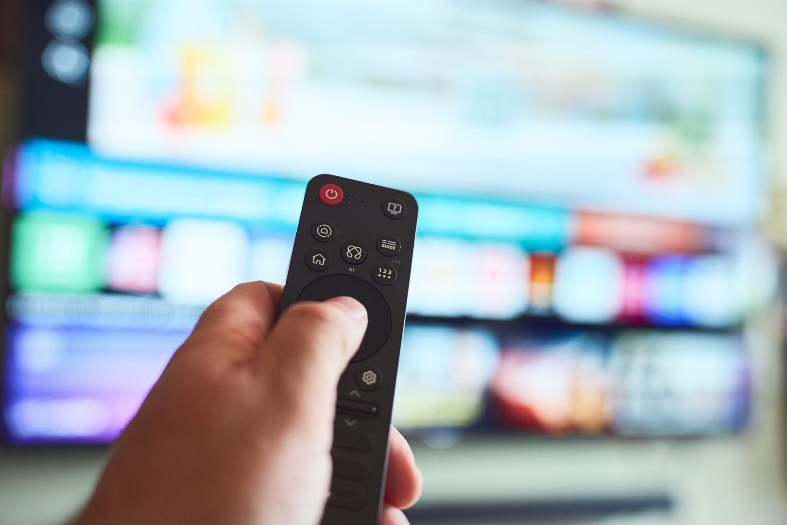 A hand holds a remote control while navigating streaming options on a large television, showcasing modern entertainment technology.